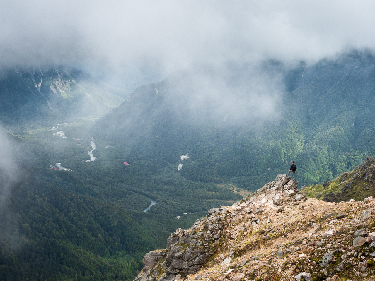 A hiker stands on a cloudy precipice on Mount Yake, a volcano in Kamikōchi (the Upper Highlands) in the Hida Mountains, Nagano Prefecture, Japan.