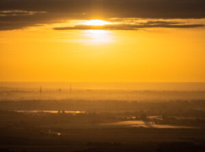 Wind turbines seen through mist at sunrise from Firle Beacon, a hill on the South Downs Way, East Sussex, England.