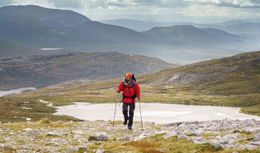 Solo hiker traversing remote Highland terrain, highlighting adventure filming capabilities for outdoor charity campaigns